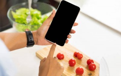 Nutrition Control Concept. Female hands holding smartphone on healthy food background on white table, top view, mock up